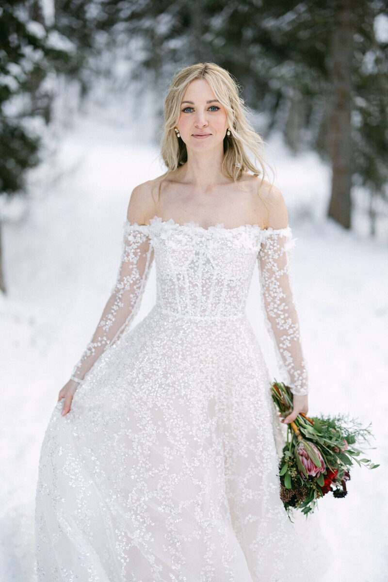 A bespoke image of a bride walking gracefully through the snow at Lake Louise. Captured on a gorgeous winter day, she holds a stunning bouquet, surrounded by the serene beauty of the snowy landscape