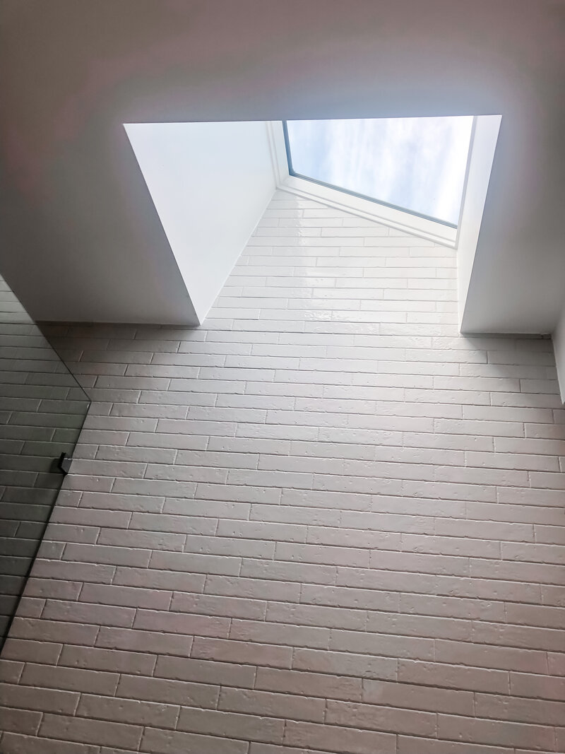 Experience the elegance of bespoke interior design in Newcastle, NSW with a view of a white brick wall featuring a triangular skylight that bathes the space in natural light. This luxury home design effortlessly combines style and functionality.