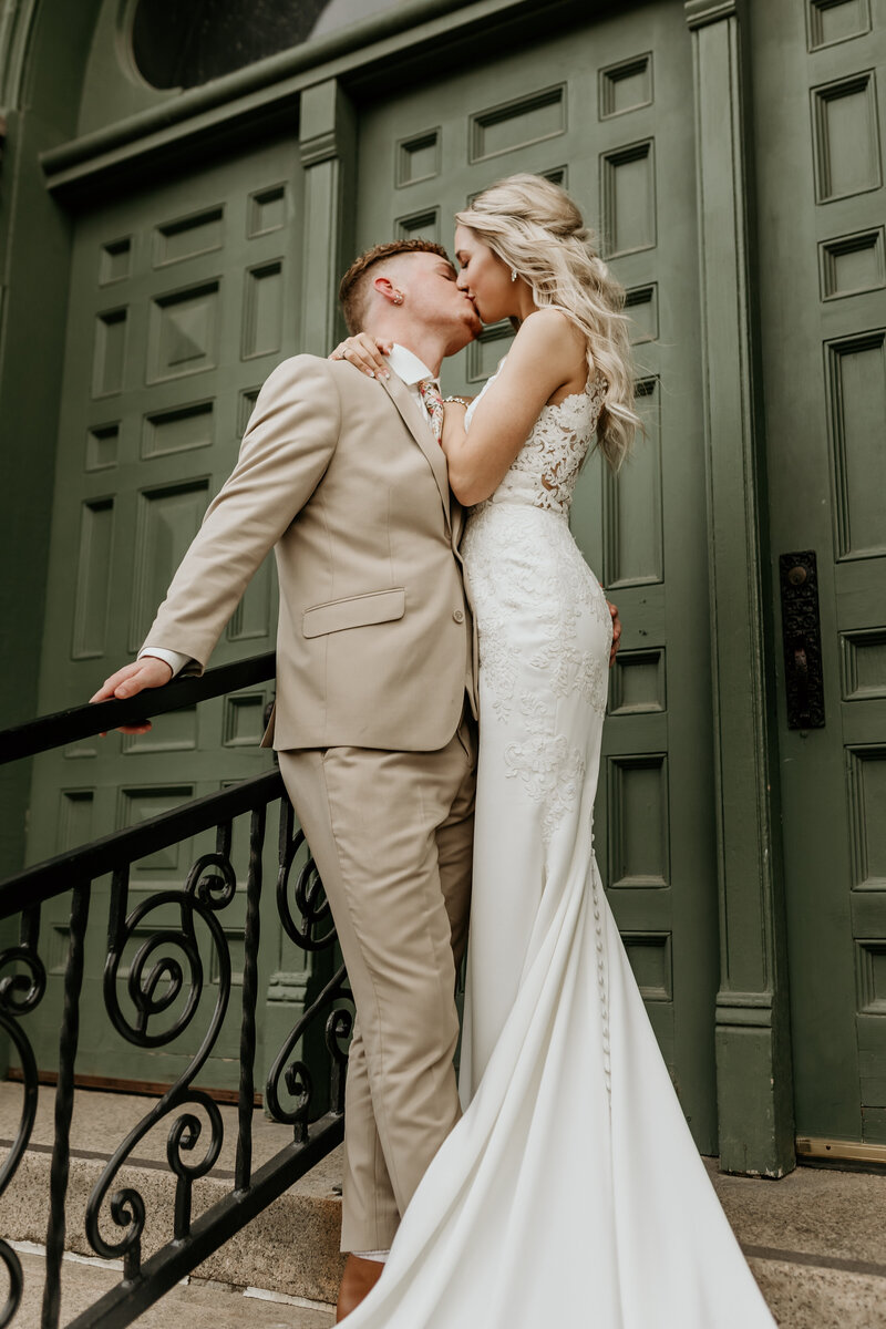 bride and groom kiss in front of green doors