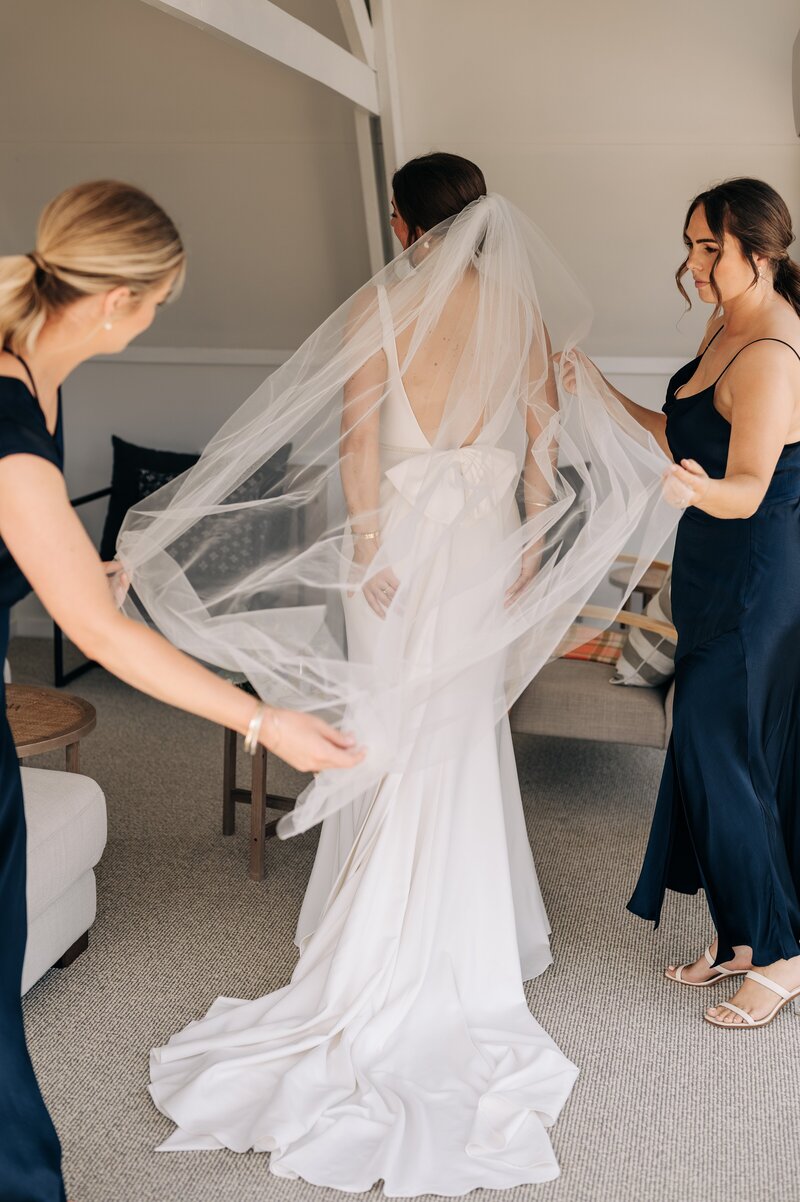 bridesmaids in navy put veil on bride in akaroa airbnb on wedding day