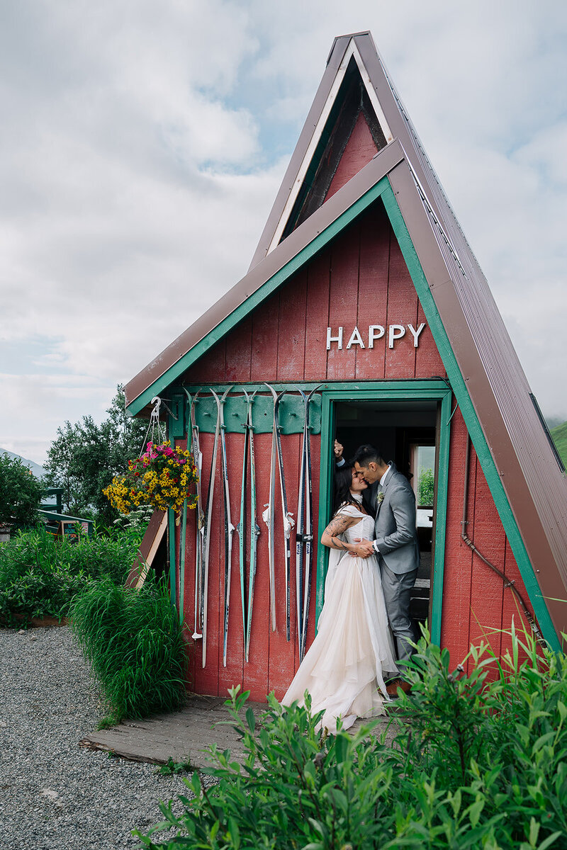 A bride and groom stand in the doorway of a cabin and kiss