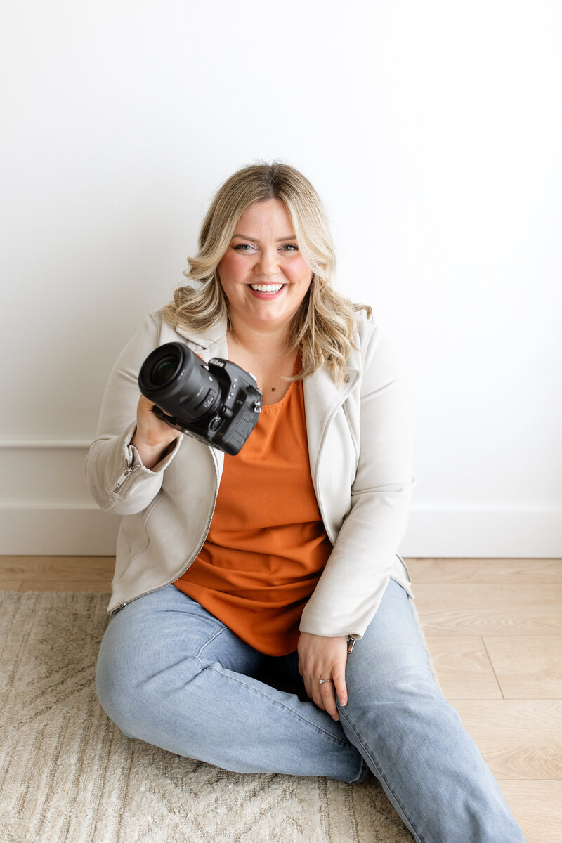A branding solo shot of a photographer with her camera while sitting on the floor.