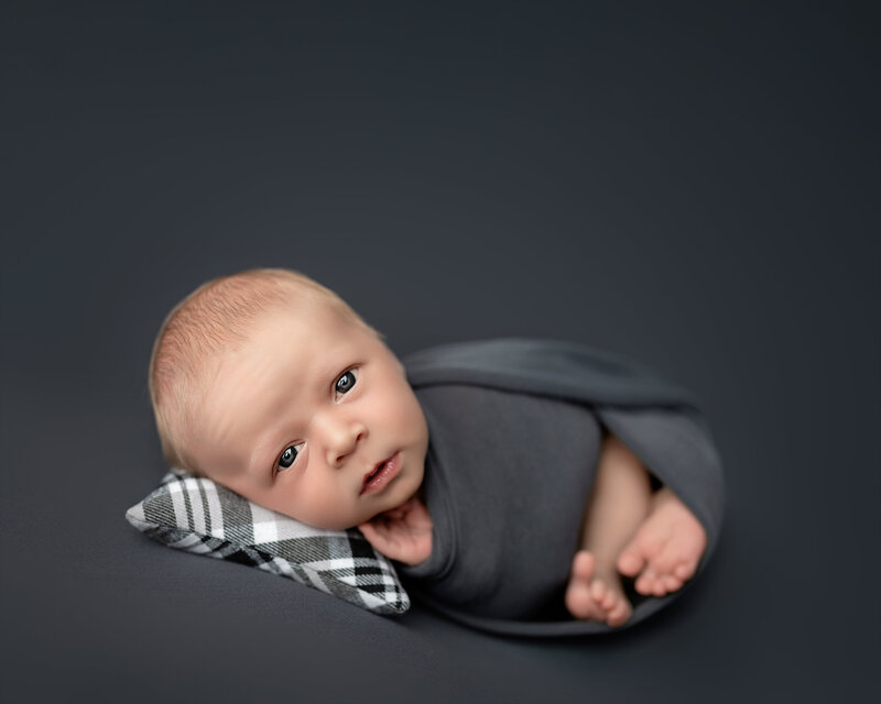 Curious eyes and soft wrap – a newborn boy in huck finn pose on dark grey.
