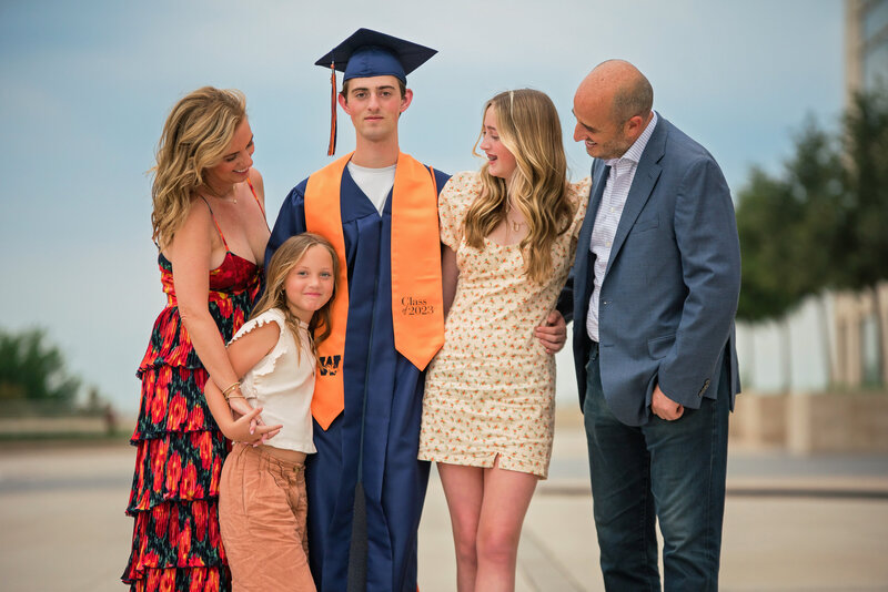 A graduation senior in a cap and gown poses for family photos. 