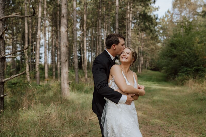 groom hugging bride in a forest while kissing her head