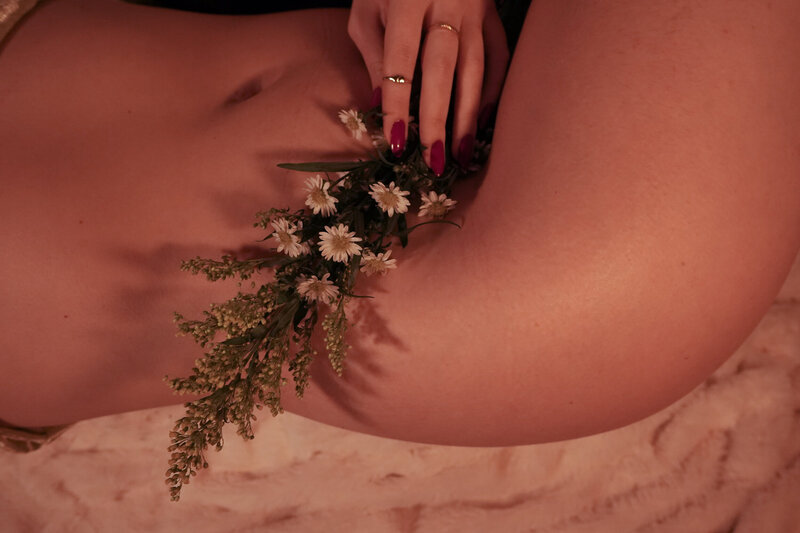 A woman with short, curly brown hair stands with her back facing the camera, her hands wrapped around her body. Colorful flowers spill out of the back pocket of her jeans, adding a playful and whimsical touch to the image. The woman's relaxed pose and carefree attitude convey a sense of ease and freedom. [Nicole QW]