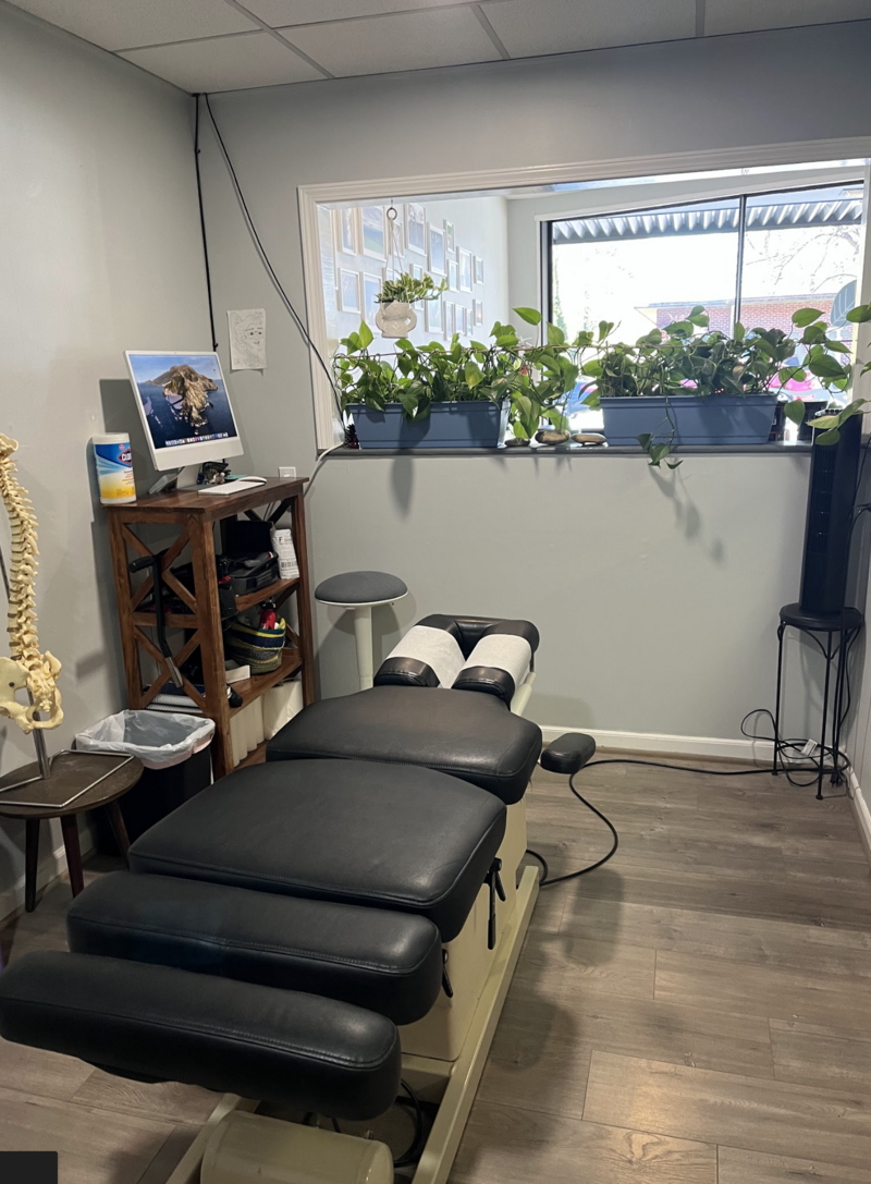 An open treatment room and table, at Thrice Chiropractic, framed by plants and natural sunlight.