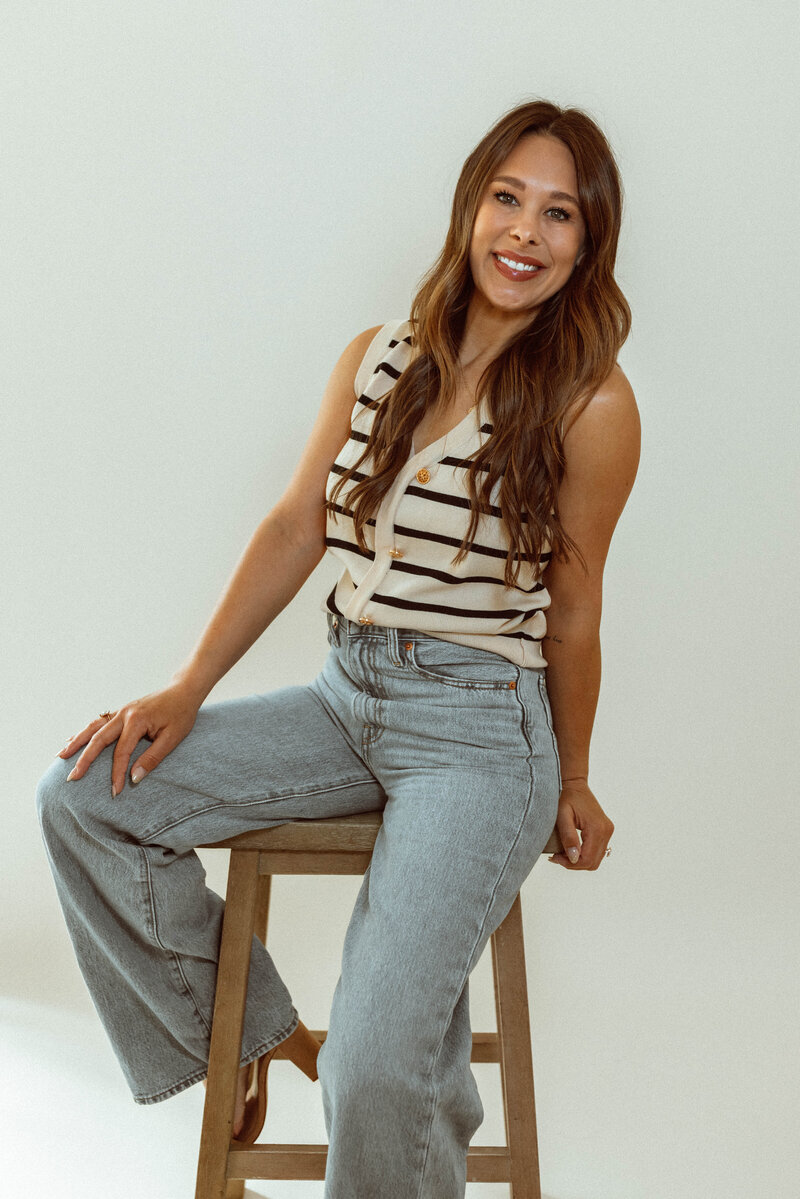 Photographer Michelle Close sitting on a stool in an all white studio. 