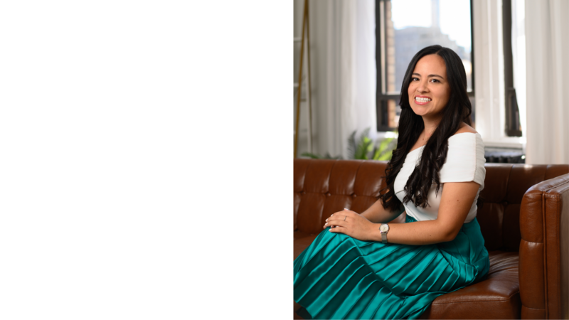 Latina woman founder smiling and sitting on brown leather couch with her legs crossed wearing a white top and turquoise skirt