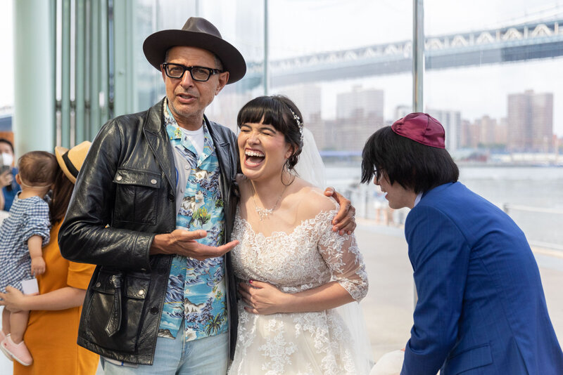 A bride laughing as Jeff Goldblum puts his arm around her.