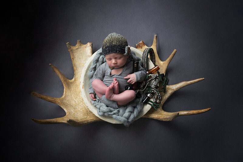A tribute to heritage and the outdoors—this newborn portrait features a hunting-inspired antler setup and rustic textures.