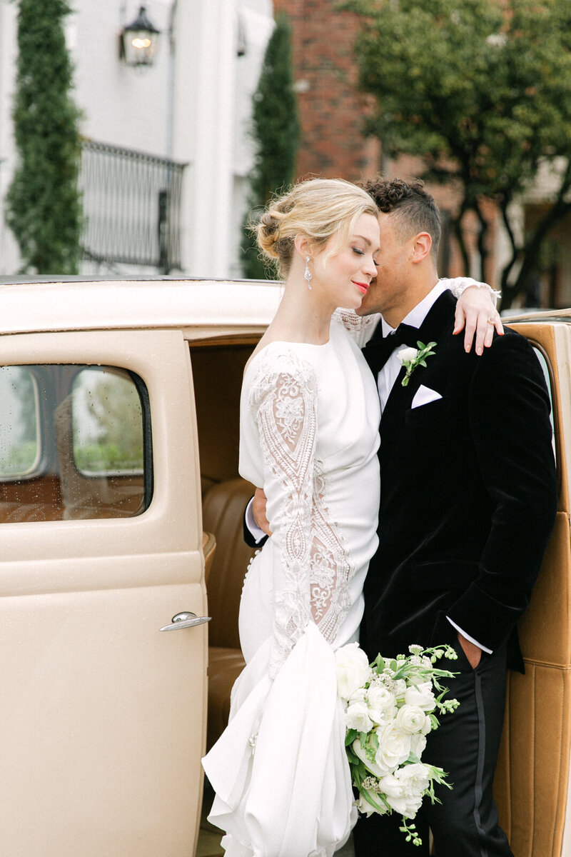 Intimate portrait of a groom giving a kiss to his bride near vintage car in front of The Mason 