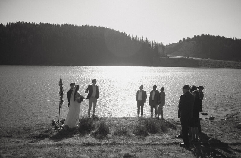 A couple stands at an alpine lake during their Colorado elopement ceremony with their closest family and friends
