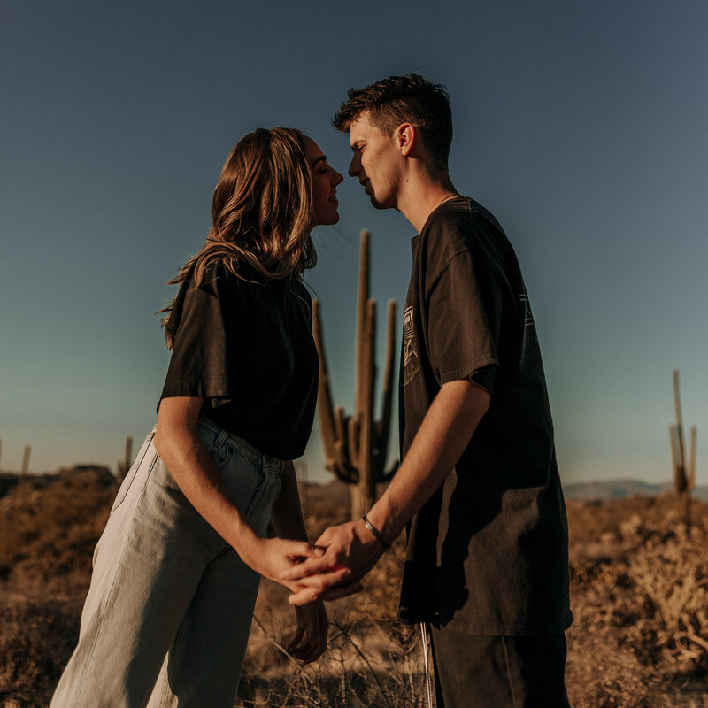 couple in front of saguaro cactus holding hands in black shirts and jeans