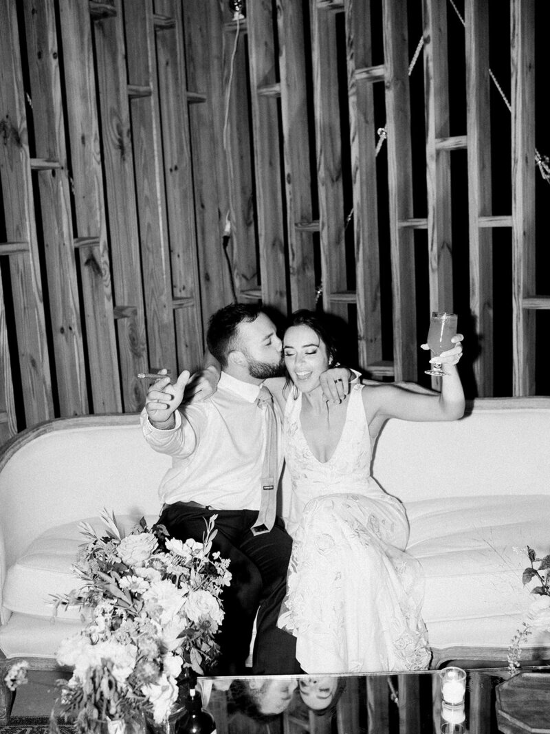 Black and white photo of groom kissing bride in a candid, casual moment during reception