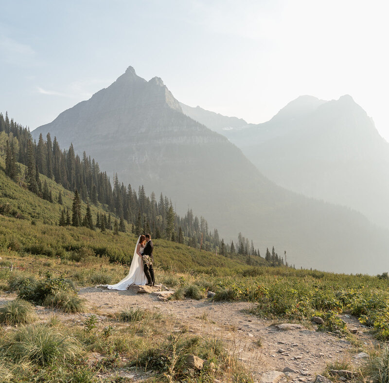 A couple shares an intimate moment during their Glacier National Park elopement, surrounded by Montana’s alpine meadows and mountain peaks, captured in soft golden light by Sydney Breann Photography.