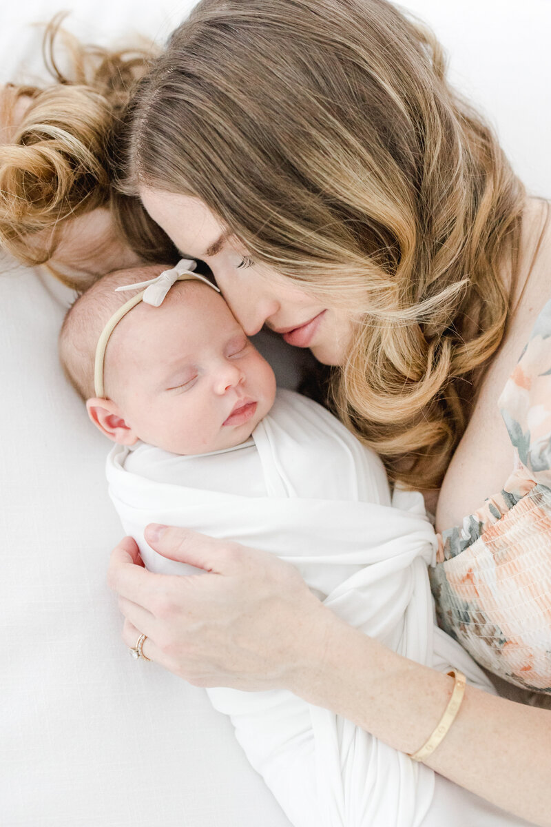 New mom snuggles her sleeping, swaddled newborn baby girl during newborn portrait photography session