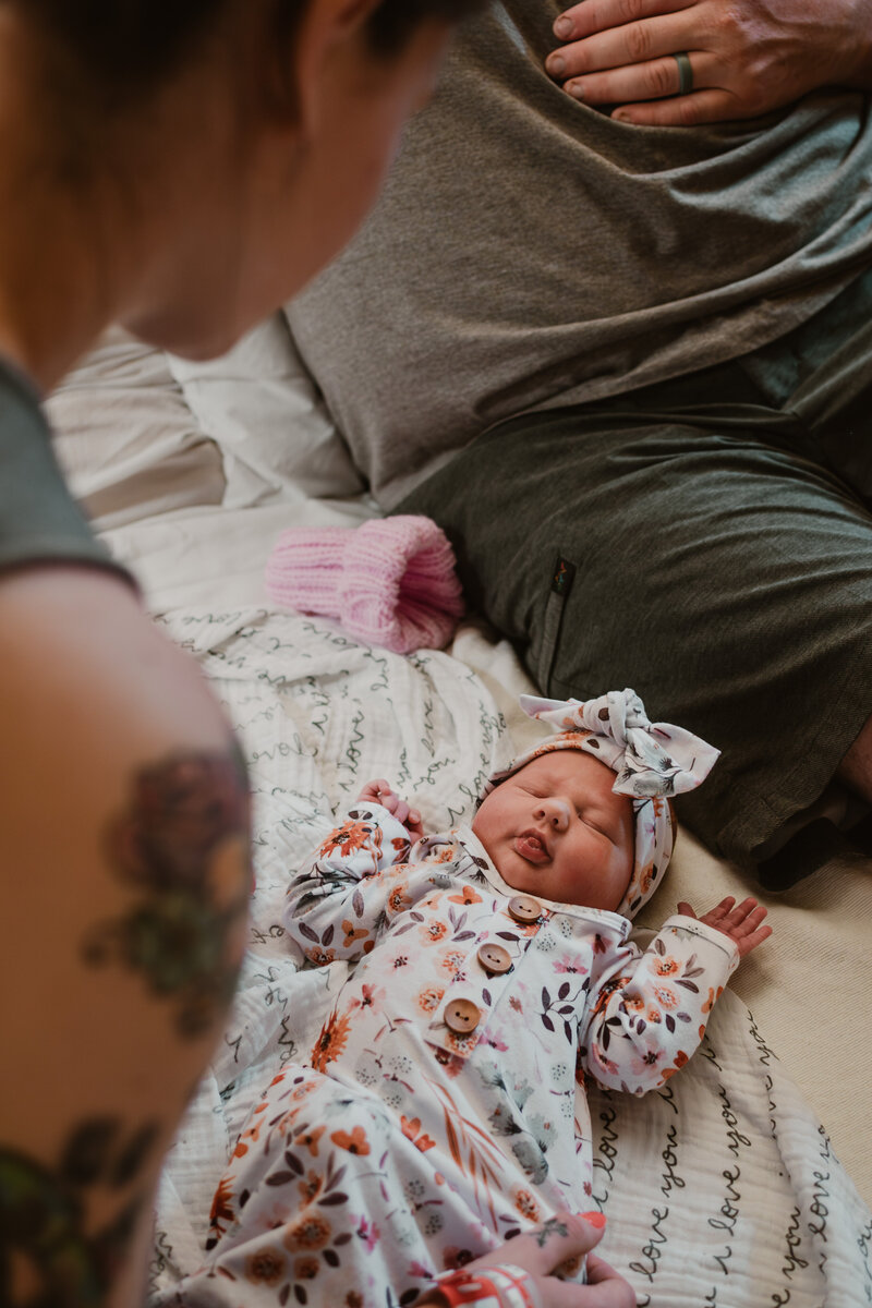 Fresh 48 photograph of mom dressing baby in pink sleeper on hospital bed white dad is sitting next to her in Annapolis Maryland photographed by Bethany Simms Photography