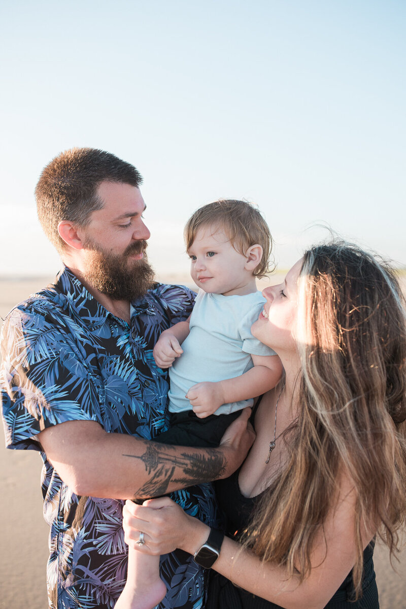 Family of 3 snuggled together during family photos on the beach near Seaside, Oregon