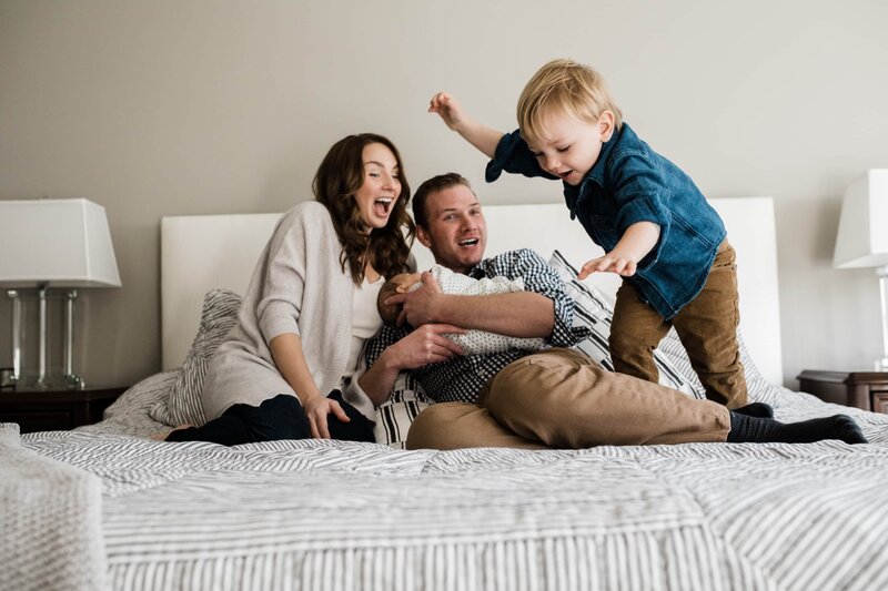 A family enjoying playful time together on a bed, captured by a skilled Pittsburgh PA photographer.