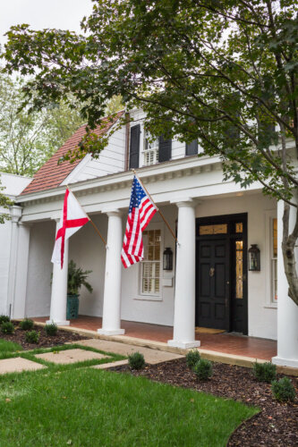 Image of southern home painted white, black front door, columns, american flag
