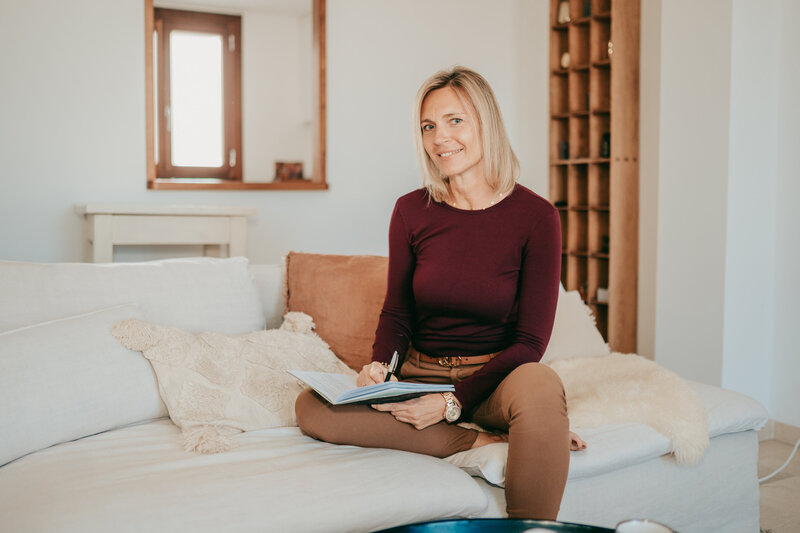 Sylke mit ihrem Notizbuch auf dem Sofa sitzend