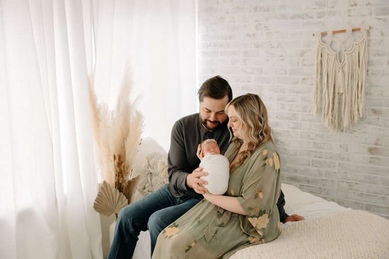 newborn with mom and dad on bed at studio