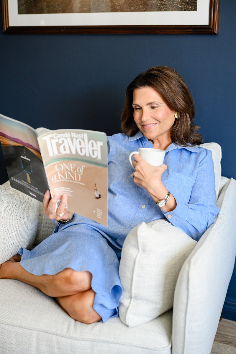 Luxury travel agent Malia Round sitting on a couch reading  a travel magazine