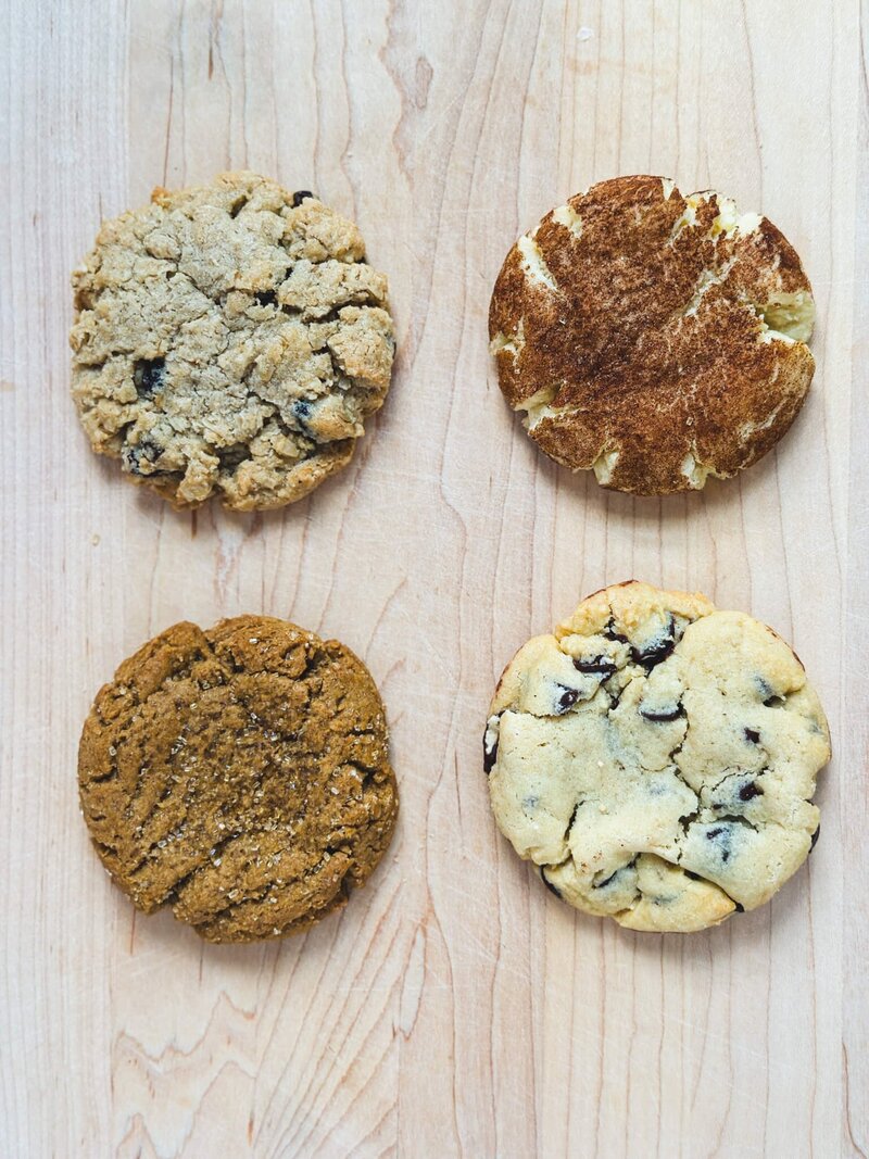 Four delicious homemade cookies featuring chocolate chip, oatmeal raisin, ginger molasses, and snickerdoodle flavors.