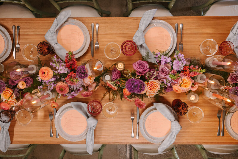 Overhead shot of reception table full of vibrant purple, orange and pink flowers and bright decorations.