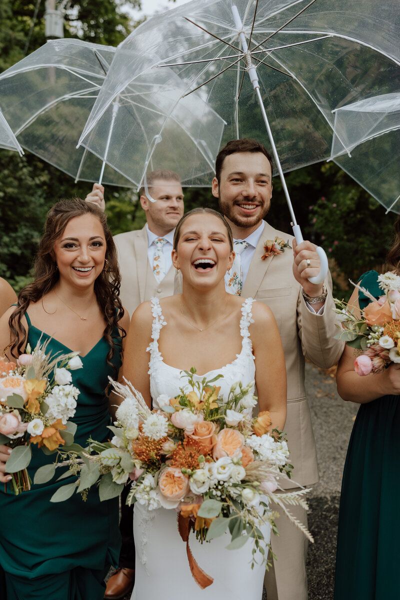 bridal couple and wedding party laughing under umbrellas