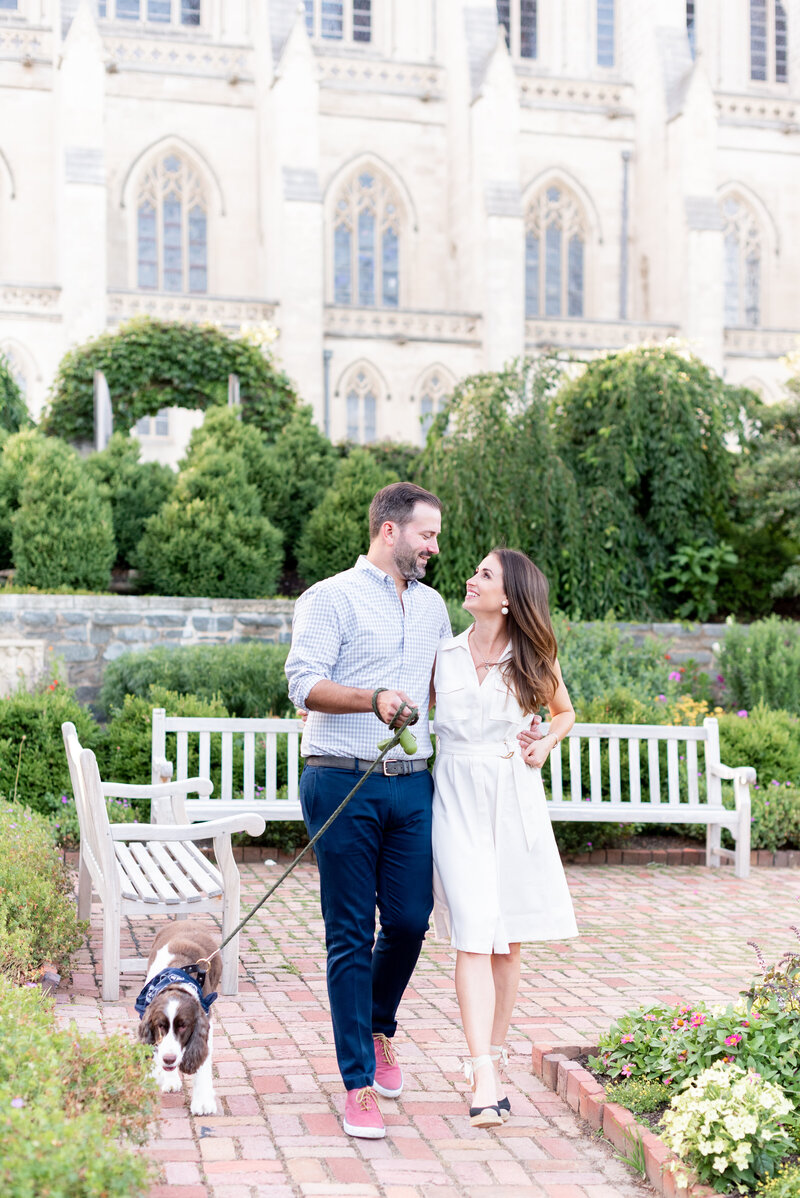 engaged couple with puppy taking engagement photos at National Cathedral engagement session