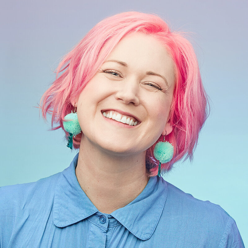 Smiling woman with pink hair against blue green gradient.