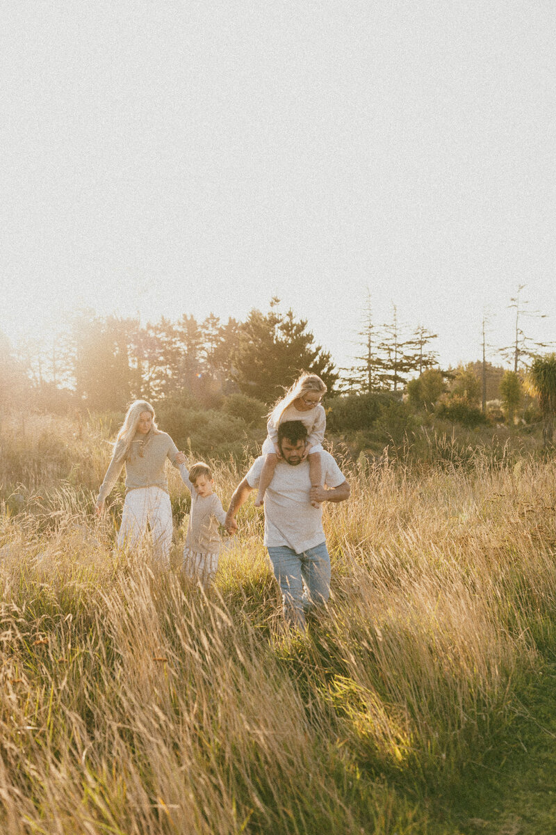 A family of four running through the long grass at sunset during a family photoshoot with Christchurch photographer Lucy Jane Photography