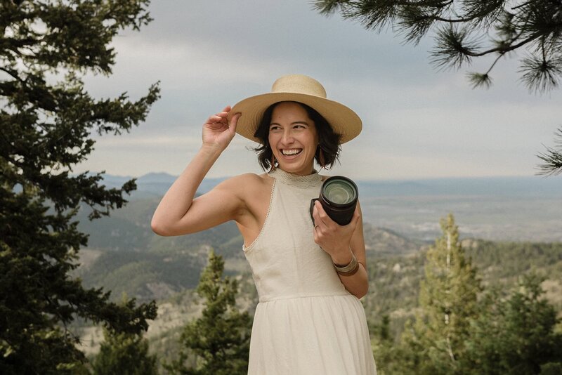 denver micro wedding photographer poses with her camera while standing  in the Colorado mountains.