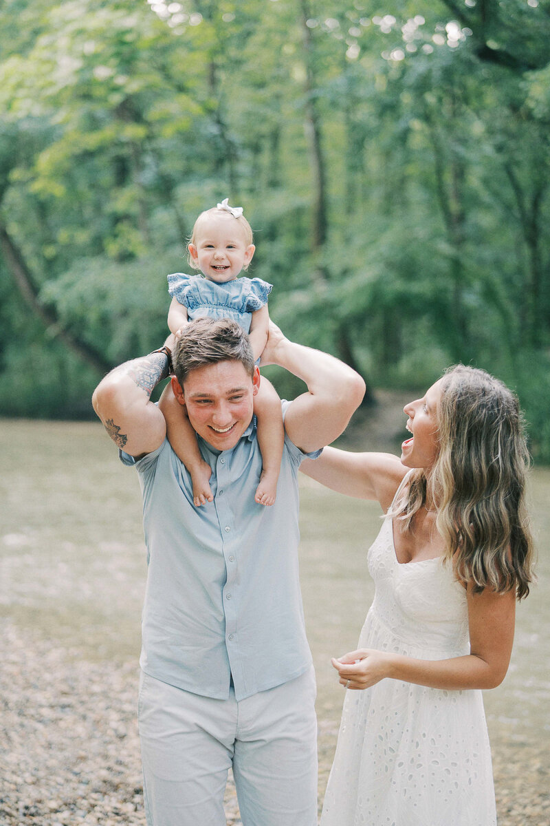 dad holds daughter on his shoulders while mom tickles her