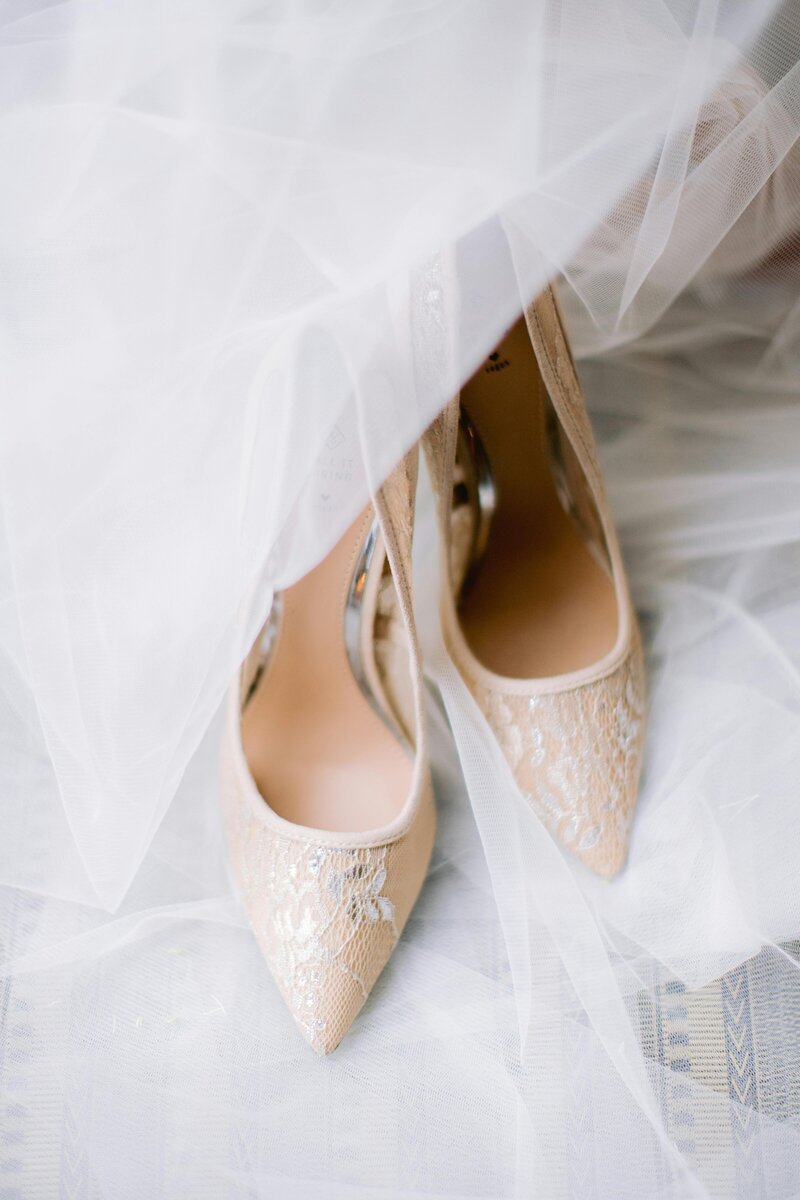 Bride's lace shoes adorned with a delicate veil draped elegantly across them, adding a touch of romance and sophistication to her wedding ensemble.