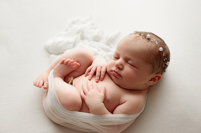 newborn baby girl wearing white and swaddled on soft white blanket