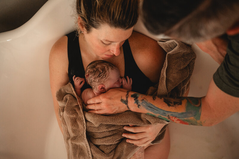 Mother cradling newborn baby wrapped in a towel after delivery — tender and emotional DFW birth photography by Poppy + Blue Photography
