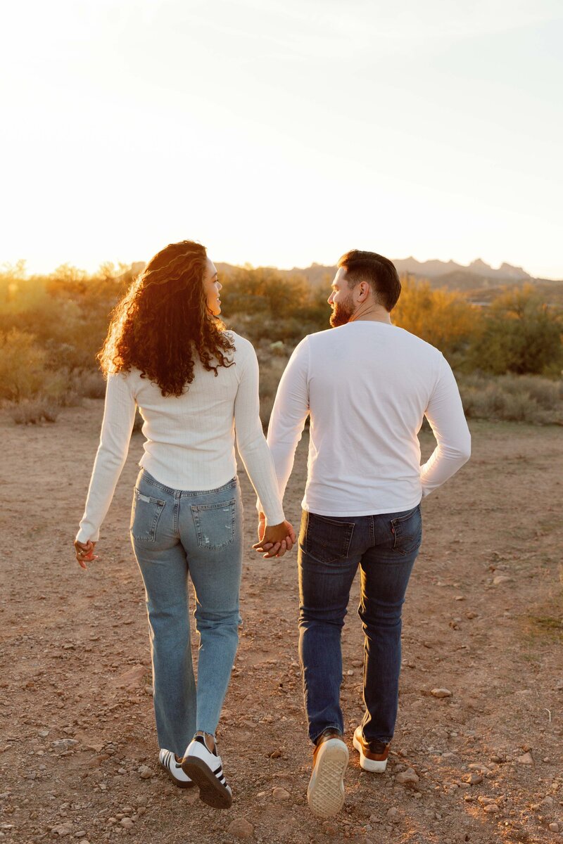 Couple walks away holding hands in the Superstition Mountains at sunset.