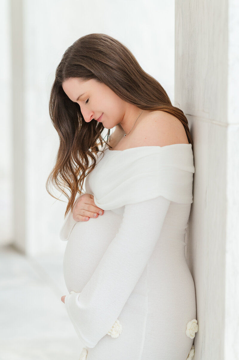 pregnant woman in white dress looking down at belly but maternity photographer york pa