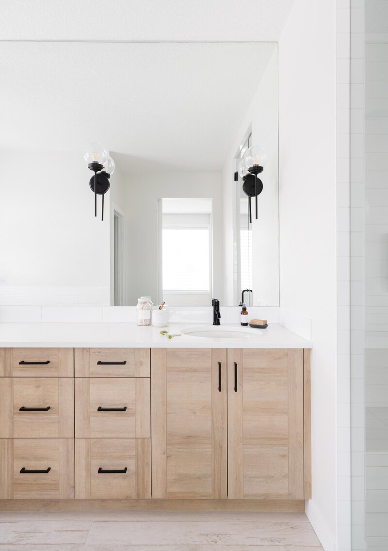 large mirror with black sconces, oak bathroom cabinets with black handles, white countertops
