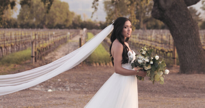 A wedding video still frame of a Beautiful bride holding her bouquet with wedding dress veil flowing behind her at a California winery wedding.