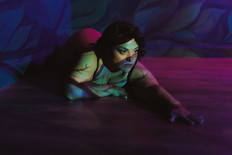 Conceptual neon boudoir photo of a woman crawling forward under moody colored light projections in a Tampa studio