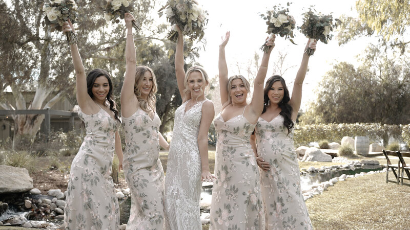 wedding bridal party is cheering with their hand up in the air while grabbing their bouquets.