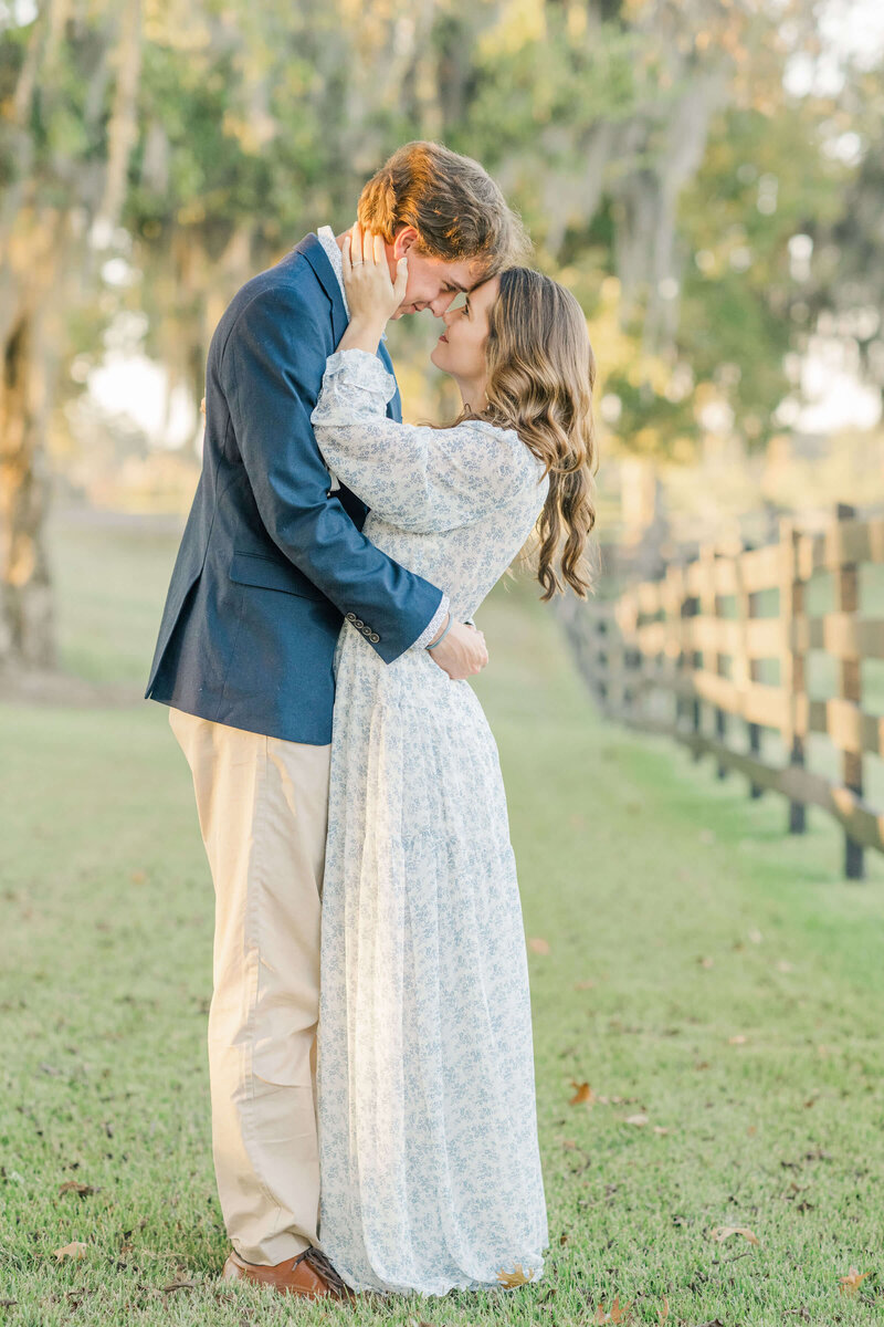 Engaged couple holding each other standing under a tree looking into each others eyes