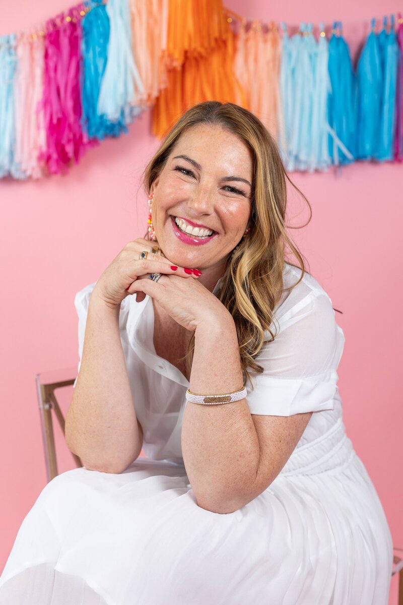 woman with dark hair in white dress sitting with bright streamers