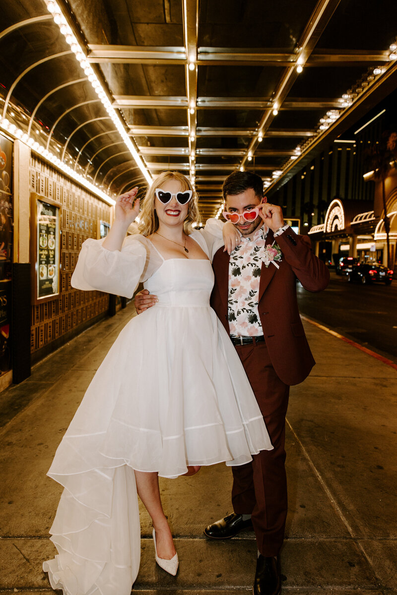 An eloped couple poses with sunglasses with Vegas lights