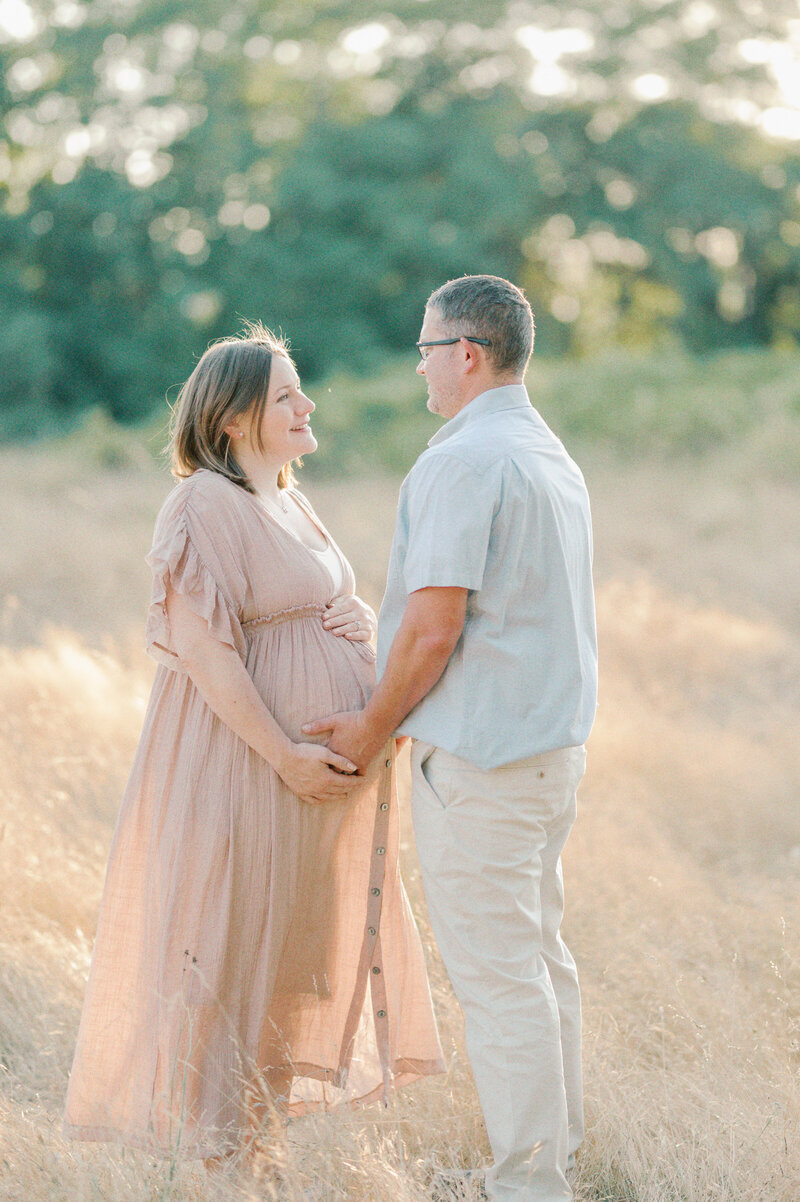 mother and father expecting baby girl posing in a field