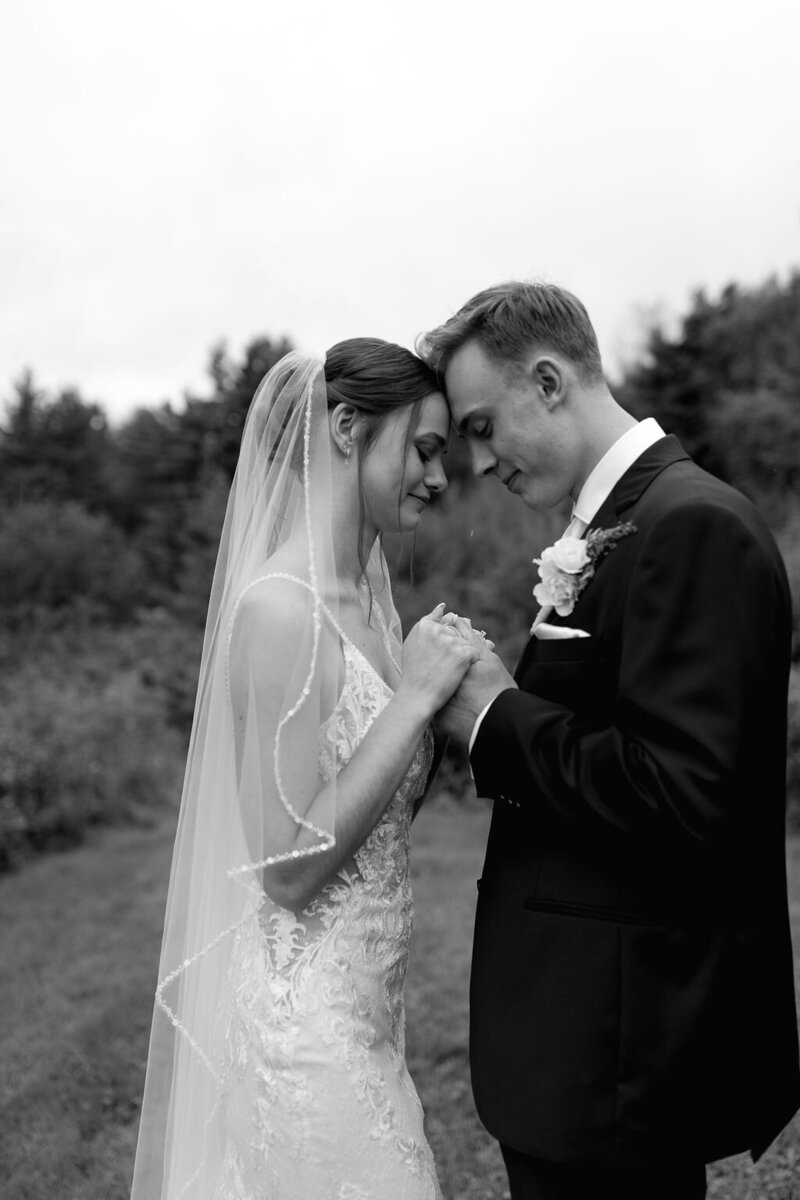 Black and white intimate wedding photo of a romantic moment between newlyweds outdoors with bride in lace and veil.